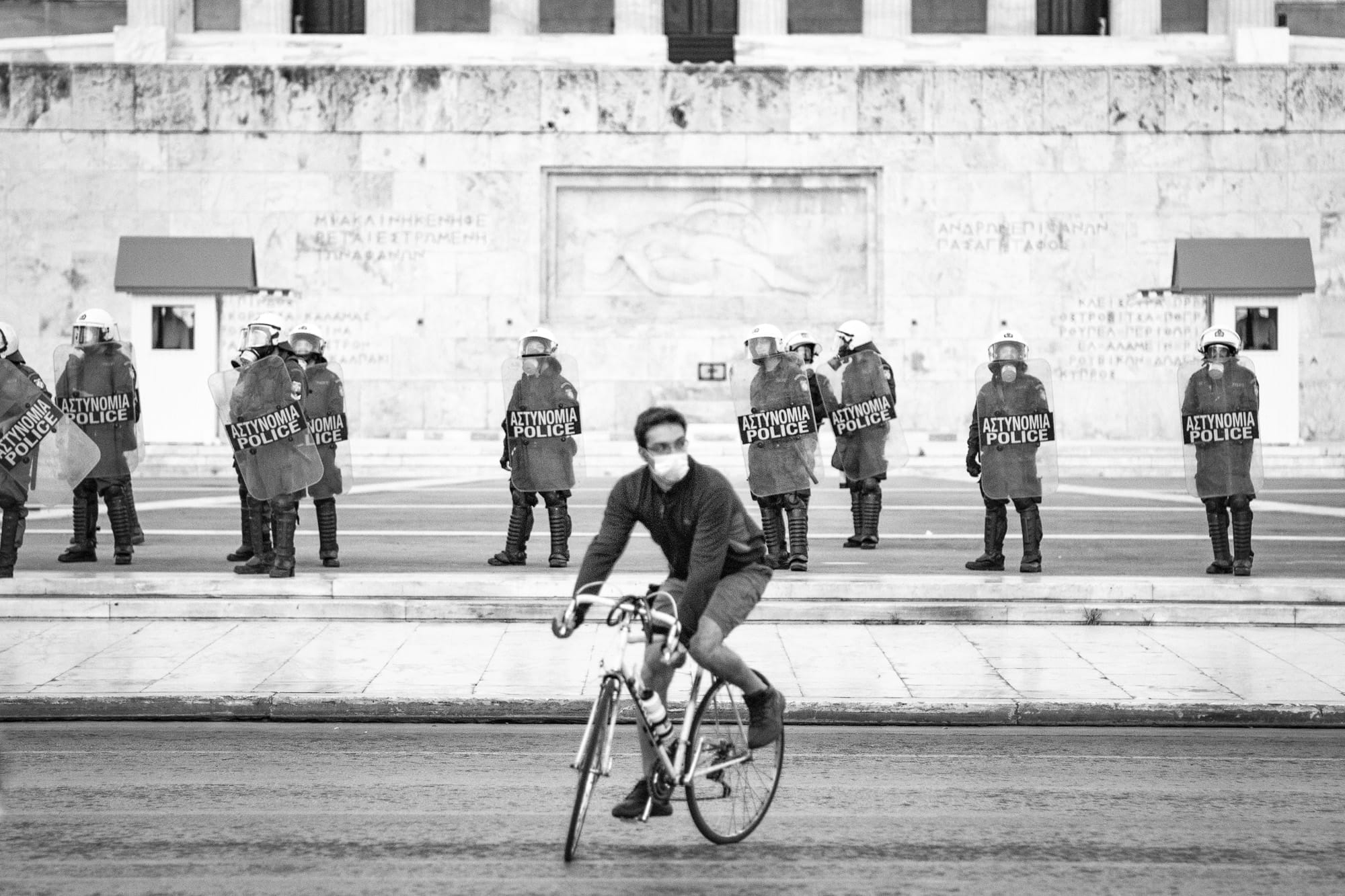 Masked cyclist passes Greek riot police in front of the Hellenic Parliament in Syntagma, Athens